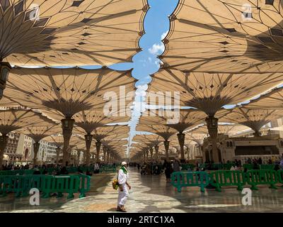 Medina, Arabia Saudita - 22 agosto 2023: I pellegrini camminano sotto ombrelli giganti nel complesso della Moschea Nabawi. Baldacchino a Masjid Nabawi a Medina, in Arabia Saudita Foto Stock