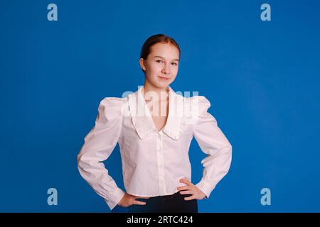 colpo alla testa adolescente sorridente in camicia bianca che guarda lo sfondo dello studio isolato in blu chiaro Foto Stock