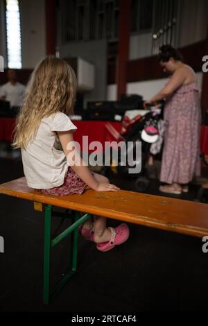 Berlino, Germania. 12 settembre 2023. La bambina Emilya siede su una panchina di fronte a sua madre durante il periodo di servizio in un centro di distribuzione "Laib und Seele" (Loaf and Soul) gestito dal Berliner Tafel nella comunità protestante della chiesa di Paulus. Credito: Sebastian Christoph Gollnow/dpa/Alamy Live News Foto Stock