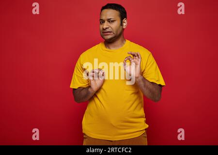 emotivo indiano con abiti casual e luminosi che fanno disgustata espressione su sfondo rosso Foto Stock