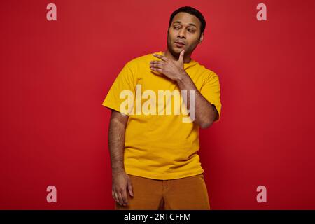 uomo indiano altezzoso e confidente in abiti casual e luminosi che gridano su sfondo rosso in studio Foto Stock