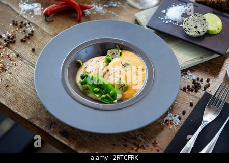 Capesante con schiuma di gamberi, crema di cavolfiore e piselli verdi su un piatto. Delizioso e salutare primo piano di pesce servito per pranzo su un tavolo in stile moderno Foto Stock