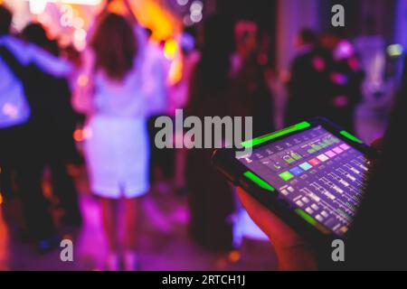 Visione del tecnico dell'illuminazione con tablet, dell'operatore che controlla il suono e la luce durante un concerto dal vivo durante la trasmissione dello spettacolo sul palco, del tecnico con profe Foto Stock