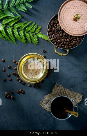 Caffè filtro dell'India meridionale servito in un bicchiere di ottone tradizionale o in una tazza con chicchi di caffè crudo tostati. Caffè tradizionale filtrato servito in una tazza di ottone Foto Stock