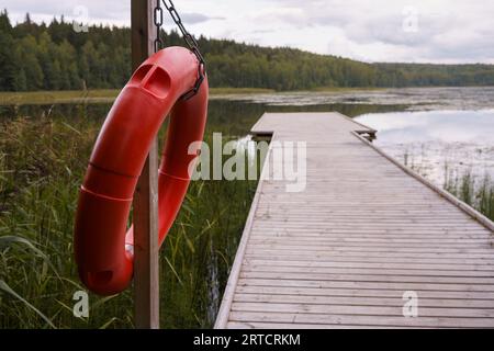 Boa ad anello rosso appesa a un palo, accanto ad un molo di legno Foto Stock