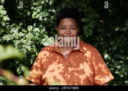 Ritratto frontale di una donna nera anziana sorridente che guarda la fotocamera contro il verde all'aperto Foto Stock