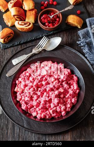 Insalata cremosa di mirtilli rossi con mini marshmallow, mela fresca e noci pecan in ciotola nera su tavolo di legno scuro con rotoli alla cannella, ricetta di Natale, ve Foto Stock