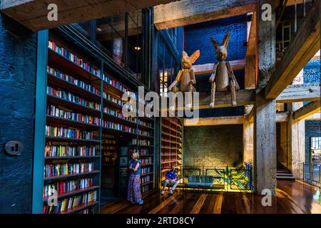 Una donna sta di fronte a una libreria. Un uomo siede su una panchina. Due grandi figure di coniglio di legno si trovano su una trave. La scena è ambientata in quello che oggi è Cafe Stamba, un'ex stamperia a Tbilisi, Georgia Foto Stock