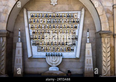 Muro commemorativo della sinagoga di Tbilisi con ritratti di uomini. I ritratti sono montati su una struttura che assomiglia a un rotolo della Torah. Una Stella di David è scolpita nella pietra sopra i ritratti. Una menorah è posta sotto i ritratti. Il muro commemorativo si trova a Tbilisi, Georgia Foto Stock