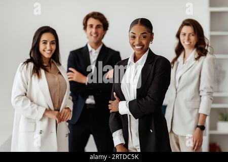 Team aziendale multirazziale di successo con leader donna di colore in piedi in ufficio e sorridente alla telecamera Foto Stock