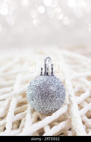 Il giocattolo di Natale di Capodanno in argento su sfondo realizzato a mano con fili. Sfocatura bokeh, messa a fuoco morbida. Verticale. Copia spazio Foto Stock