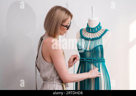 L'artigiana intreccia fili verdi per creare un abito in macrame in un atelier di moda donna crea abiti Foto Stock