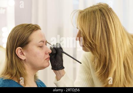 Il master disegna la forma delle sopracciglia con vernice bianca prima della correzione delle sopracciglia. Industria della bellezza. Foto Stock