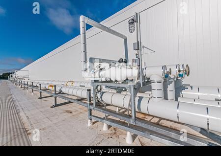 Tubazioni isolate bianche montate sul tetto di un impianto di stoccaggio a freddo, per il trasporto di liquidi e gas nella refrigerazione a ciclo di ammoniaca. Foto Stock