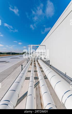 Tubazioni isolate bianche montate sul tetto di un impianto di stoccaggio a freddo, per il trasporto di liquidi e gas nella refrigerazione a ciclo di ammoniaca. Foto Stock