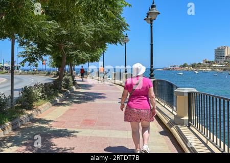 St Julians, Malta - 2 agosto 2023: Persona che cammina lungo la passeggiata intorno alla baia di St Julian Foto Stock