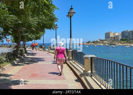 St Julians, Malta - 2 agosto 2023: Persona che cammina lungo la passeggiata intorno alla baia di St Julian Foto Stock