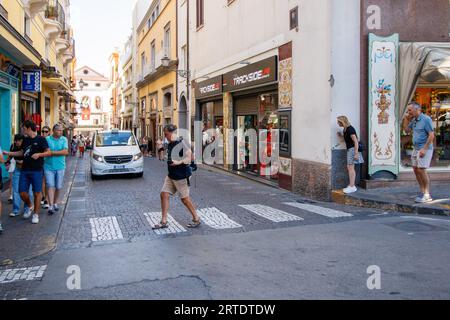 La stretta via Luigi de Maio che ha solo un marciapiede su un lato. L'incrocio conduce a via S Cesareo, una stretta stradina fiancheggiata da negozi turistici nel cuore di Sorrento. Sorrento è una città costiera dell'Italia sud-occidentale, affacciata sul Golfo di Napoli, sulla penisola sorrentina. Arroccato sulla cima di scogliere che separano la città dai suoi affollati porticcioli, è noto per le ampie viste sull'acqua e Piazza tasso, una piazza alberata da caffetterie. Foto Stock