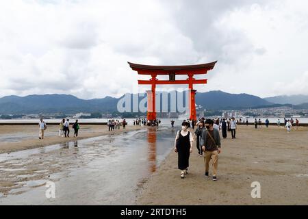I turisti si pongono di fronte a un gigantesco ingresso "torii" al Santuario di Itsukushima sull'isola di Miyajima a Hatsukaichi, nella prefettura di Hiroshima, nel Giappone occidentale. Il santuario di Itsukushima, situato sull'isola di Miyajima a Hatsukaichi, nella prefettura di Hiroshima, in Giappone, è un sito patrimonio dell'umanità dell'UNESCO, rinomato per la sua bellezza mozzafiato e le sue caratteristiche architettoniche uniche. Questo santuario shintoista è famoso soprattutto per la sua porta torii "galleggiante", che sembra emergere dall'acqua durante l'alta marea, creando una vista accattivante ed eterea. (Foto di James Matsumoto/SOPA Images/Sipa USA) Foto Stock