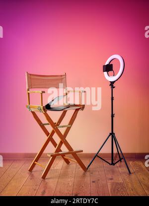 Sedia Director, illuminatori anulari, fotocamera digitale con laptop e cappelli su sfondo colorato con apparecchiature di registrazione Foto Stock