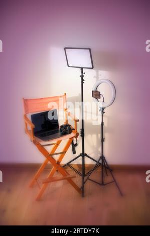 Sedia Director, illuminatori anulari, fotocamera digitale con laptop e cappelli su sfondo colorato con apparecchiature di registrazione Foto Stock