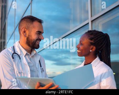 Due medici ospedalieri, una donna e un uomo, che fanno una pausa all'aperto. Guardatevi mentre sorridete. Foto Stock