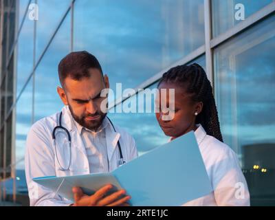 Due medici ospedalieri, una donna e un uomo, che fanno una pausa all'aperto. Controllo di alcuni documenti. Foto Stock