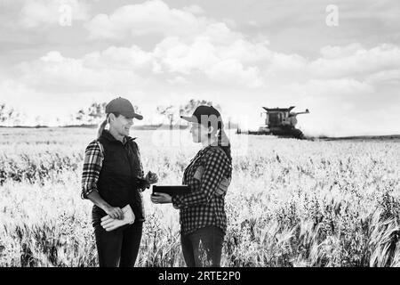 Una donna di fattoria matura in un campo che lavora insieme a una giovane donna al momento del raccolto, utilizzando software agricoli avanzati su un pad, con un ... Foto Stock