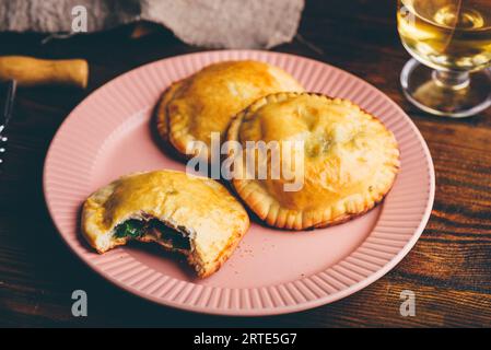 Pasticceria cotta al forno ripiena di erba cipollina e funghi su piatto con bicchiere di vino. Una torta con morso tolto Foto Stock