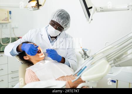 Il dentista afro-americano sta trattando la paziente femminile che è seduta in sedia Foto Stock
