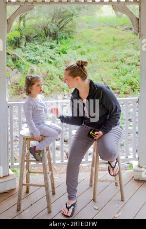 Primo piano di madre e figlia sedute su sgabelli in un gazebo presso i Kula Botanical Gardens; Maui, Hawaii, Stati Uniti d'America Foto Stock