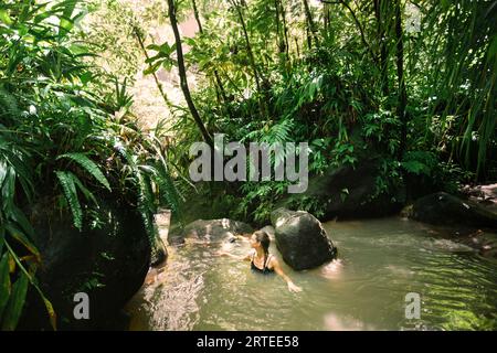 Donna che si diverte a immergersi nell'acqua calda e nelle sorgenti termali di Trafalgar Falls nella lussureggiante foresta pluviale dell'isola caraibica di Dominica a Morne Trois ... Foto Stock