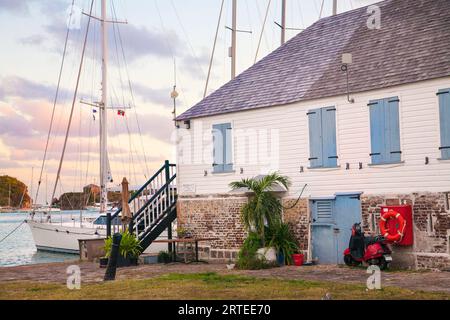 Barca a vela ormeggiata lungo la riva presso lo storico Nelsons Dockyard, con vecchia casa e fortificazione trasformata in un ristorante e negozio di articoli da regalo sull'IS... Foto Stock