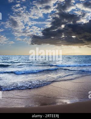 Fai surf lungo la costa di Kamaole 2 Beach al crepuscolo con una spettacolare formazione di nuvole nel cielo blu e una tonalità blu sull'Oceano Pacifico Foto Stock