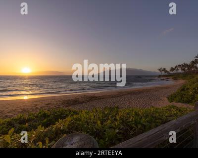 Vista dell'Oceano Pacifico e del sole dorato al crepuscolo dalla spiaggia sabbiosa di Keawakapu Beach; Kihei, Wailea, Maui, Hawaii, Stati Uniti d'America Foto Stock