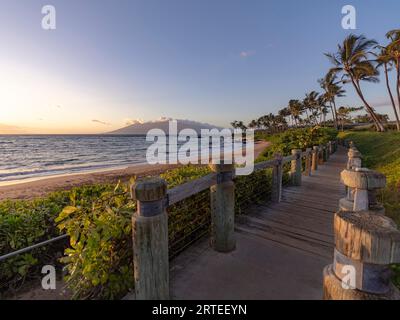 Passerella in legno lungo la riva di un resort di lusso a Keawakapu Beach con vista dell'Oceano Pacifico al crepuscolo Foto Stock