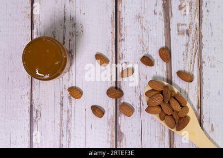 Forma di cuore fatta di più semi di mandorle accanto al legno cucchiaio di misura isolati su sfondo bianco Foto Stock