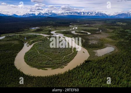 Incredibile ripresa aerea di un giro del fiume che scorre attraverso il paesaggio boschivo mentre si dirige verso le montagne vicino a Haines Junction; Yukon, Canada Foto Stock