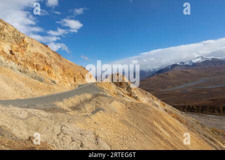 Denali Park Road erosa al passo Polychrome, in una giornata di sole d'autunno, con montagne innevate sullo sfondo nel Parco Nazionale Denali e Preser... Foto Stock