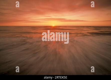 Mentre il sole illumina il cielo, un cremisi luminoso, che poi si riflette sull'acqua sottostante, declina ulteriormente oltre l'orizzonte, Beaufort se... Foto Stock