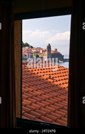 Tetto piastrellato e l'ingresso al porto attraverso una finestra; Collioure, Pyrenees Orientales, Francia Foto Stock
