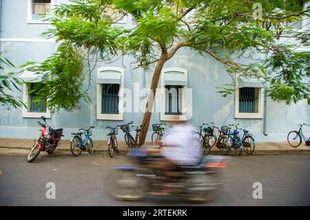 Il motociclista passa davanti alle moto parcheggiate in una strada in India; Pondicherry, Tamil Nadu, India Foto Stock