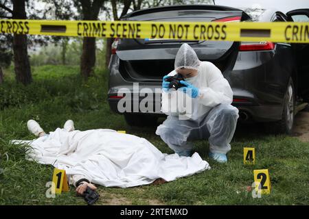 Criminologo che scatta foto di cadaveri sulla scena del crimine all'aperto Foto Stock