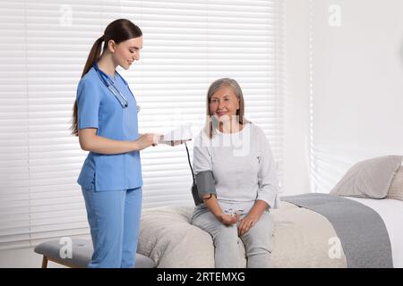 Giovane operatore sanitario che misura la pressione sanguigna della donna anziana in interni Foto Stock