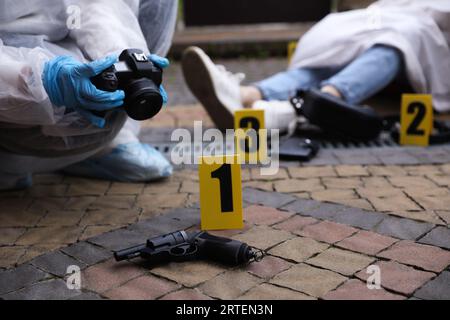 Criminologo che scatta foto di prove sulla scena del crimine con cadaveri all'aperto, primo piano. Spazio per il testo Foto Stock