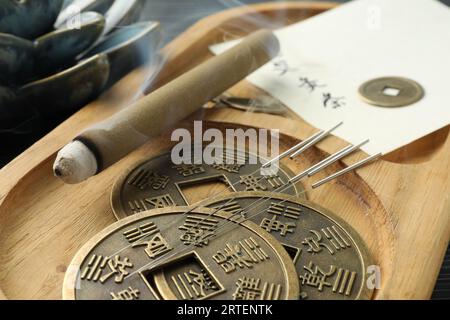 Aghi per agopuntura, bastoncino di moxa e antiche monete cinesi su vassoio di legno, primo piano Foto Stock