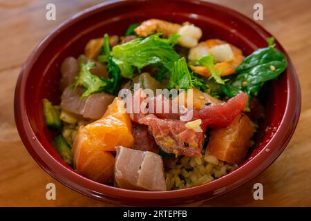 Ciotola di pesce hawaiano con salmone a dadini, tonno, gamberi e insalata isolata su fondo di legno. Foto Stock