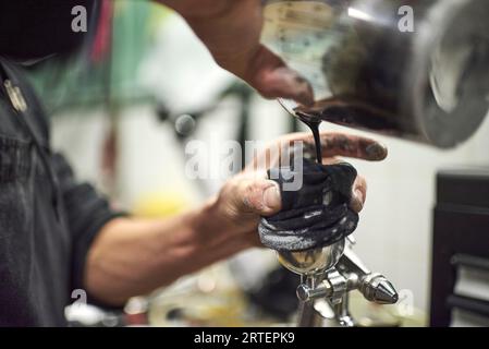 Mani di una giovane persona sconosciuta che versa vernice in un serbatoio di una pistola a spruzzo nella sua officina. Composizione della vista ad angolo ridotto con spazio di copia. Foto Stock