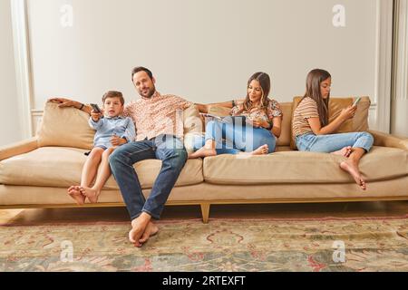 Famiglia sorridente con due bambini (8-9, 12-13) che si rilassano sul divano Foto Stock