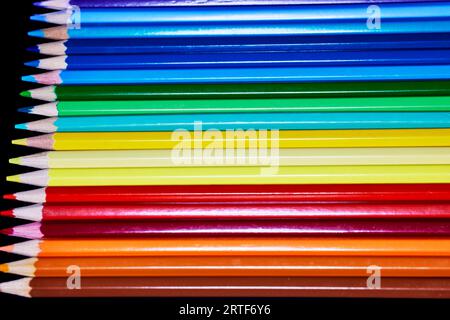 Primo piano di una fila di matite colorate isolate sul nero Foto Stock